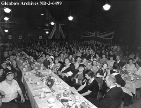 A crowd sits at packed dining tables, with British flags hung behind them.