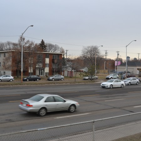 An apartment building seen across a busy street with cars passing by.
