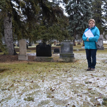A wide angle of the slush and grass at Frank Beevers' gravesite - Sheila Thomas stands to one side, holding a file of information about him.