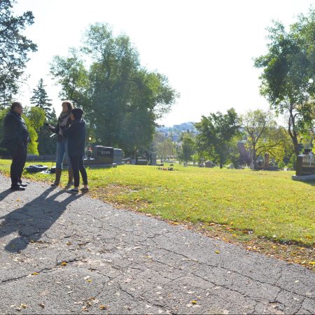 Chief Bruneau, Samantha Power, and Lauren Crazybull stand on the hill at the cemetery.