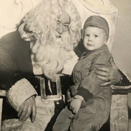 Black and white photo. Glen as a small child looks at the camera while he sits on the lap of Santa, who has a HUGE beard and belt buckle.
