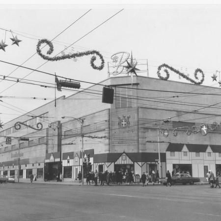 A glitzy-looking shot of the Bay at Christmas in the 1960s, with a village facade wrapped around the building. The Bay logo has a Jetsons' feel, and there are stars and pine swirls hanging from the power lines above the street.