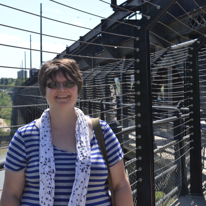 Susan stands on the sidewalk by the bridge on a sunny day