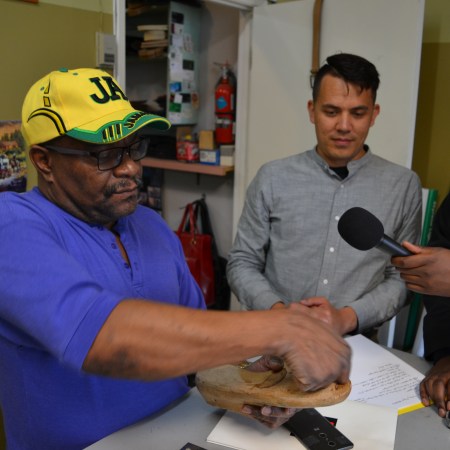 Mike Wallace wears a bright yellow and green Jamaica hat and shows off a last inside his shop