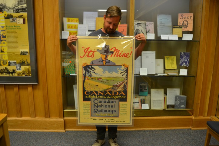 The poster reads: It's Mine! And a man holds a picture of a prairie farmstead.