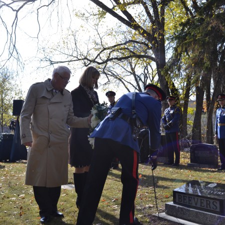 Graham and Candy stand behind a police officer laying a wreath by the new gravestone.
