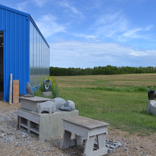 Carvings in progress of various sizes in front of a blue shed