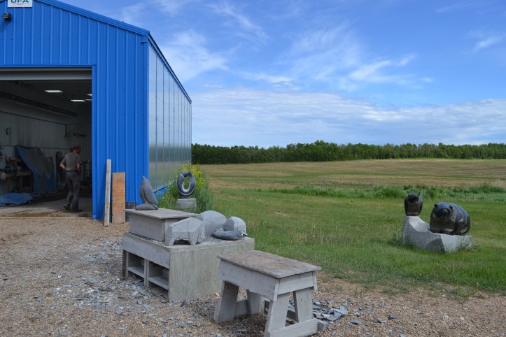 Carvings in progress of various sizes in front of a blue shed