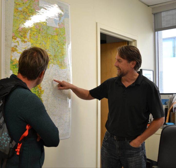 Dustin Bajer and Scott Nielsen look at a map of Alberta in Scotts office