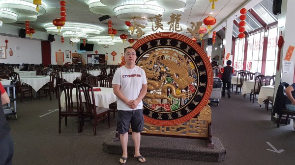 Thomas Ly stands in casual clothing in front of a circular ornament, inside Dynasty Restaurant, with social distancing arrows on the floor.