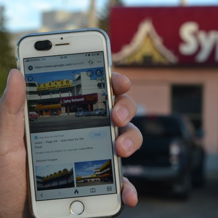 A photo of Nathan holding a phone with an image of the Mirama restaurant behind Syphay Restaurant. Behind Nathan's hand is the present-day Syphay Restaurant, with no Mirama building.