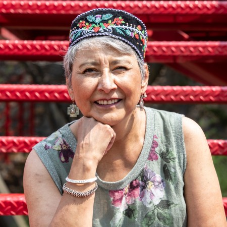 a picture of marilun dumont smiling outside, with hand under chin