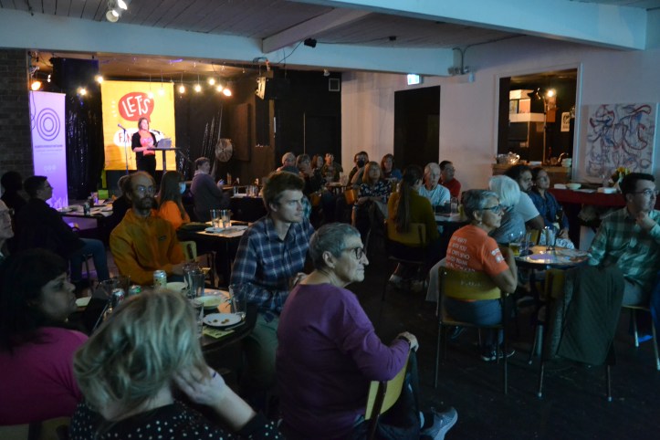 An audience in a dark room looks at a projected image off-screen