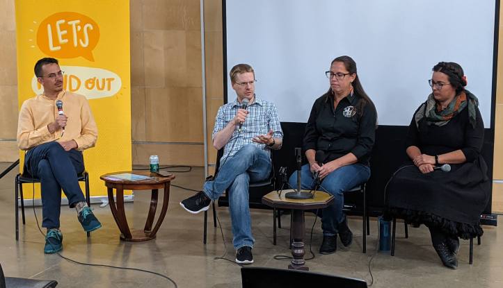 Chris speaks to panelists Mack Male, Miranda Jimmy, and Lauren Markewicz. All are seated in front of the Let's Find Out banner and a projector screen.