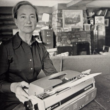 A black and white portrait of a middle-aged woman posing behind a typewriter.