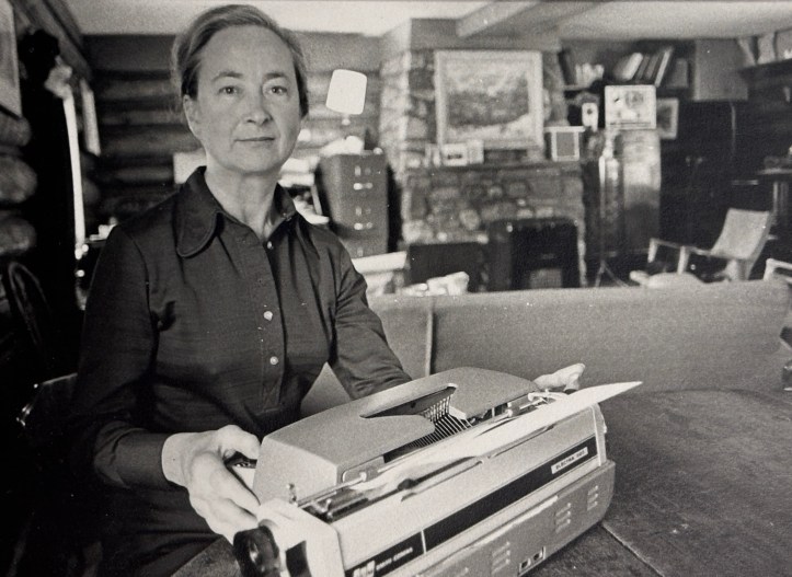A black and white portrait of a middle-aged woman posing behind a typewriter.