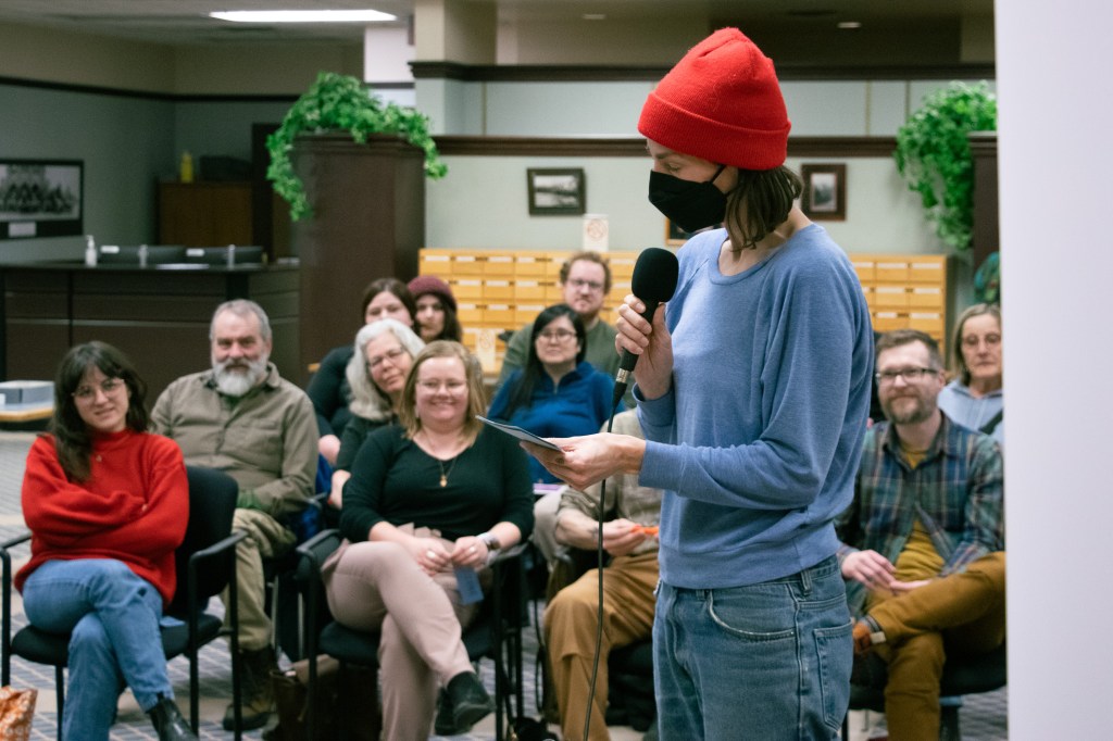 A woman in a red toque and facemask asks a question in front of the crowd.